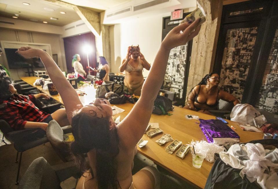 A dancer throws up her arms in front of a table of cash.