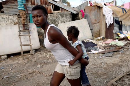 A woman carries a child as they walk in front of destroyed houses after Hurricane Matthew passes Jeremie, Haiti, October 7, 2016. REUTERS/Carlos Garcia Rawlins