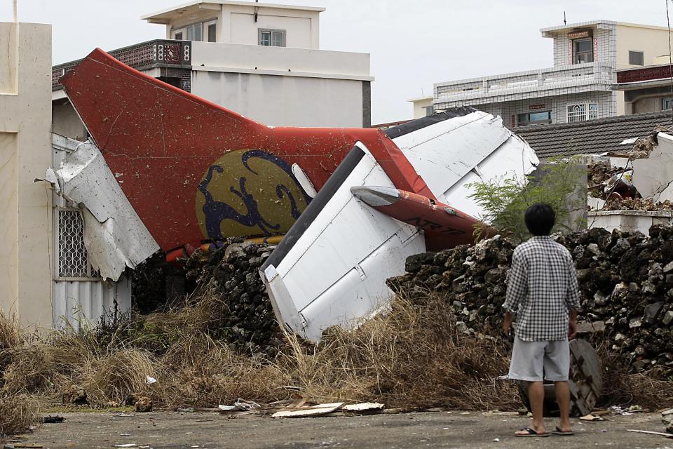 A man stands in his backyard and looks at the wreckage of a TransAsia Airways turboprop plane that crashed on Taiwan's offshore island Penghu July 24, 2014. The leaders of rivals China and Taiwan expressed condolences on Thursday for victims of the plane that crashed during a thunderstorm the previous day killing 48 people including two French nationals. (REUTERS/Pichi Chuang)