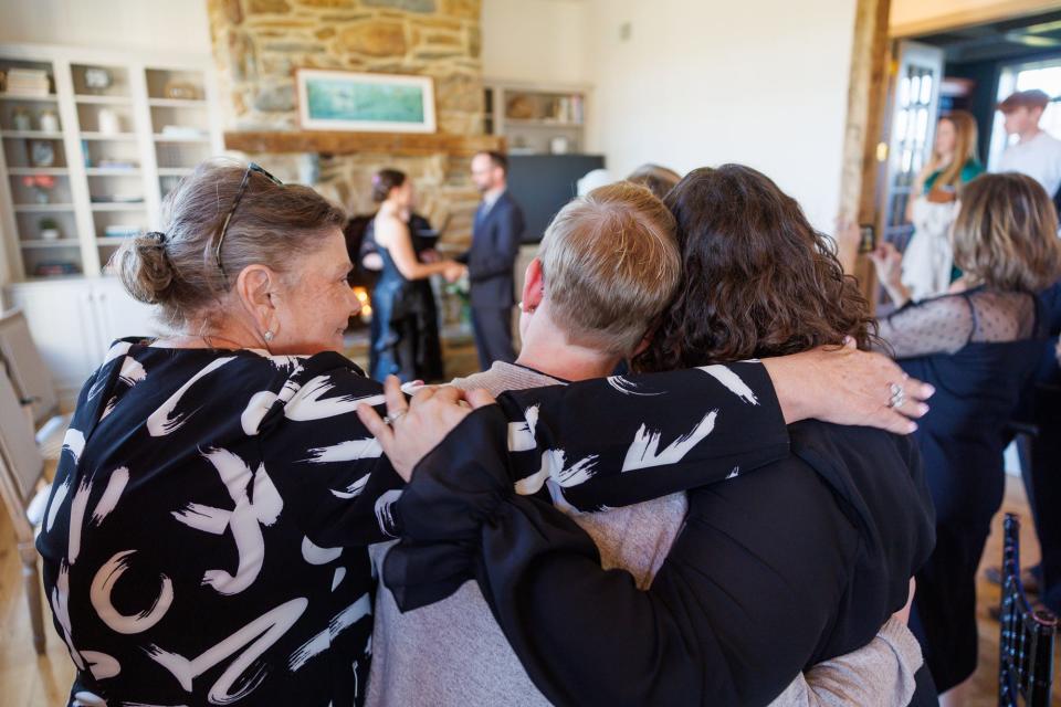 Laurie Dennis, mother of the bride, left, embraces Mackenzie Imperant, center, and Becky McClellan, right, as they watch a surprise wedding ceremony, Friday, March 29, 2024, at Wynridge Farms in York Township.