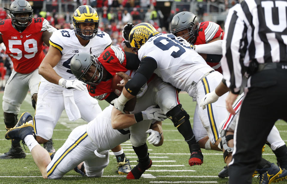 FILE - Ohio State quarterback J.T. Barrett, center, runs for a first down as Michigan defenders Chris Wormley, left, Matthew Godin, and Ryan Glasgow make the tackle during the second half of an NCAA college football game, Nov. 26, 2016, in Columbus, Ohio. The Buckeyes had a fourth-and-1 on their possession, and coach Urban Meyer went for it instead of kicking for a tie. J.T. Barrett just barely made the line to gain and the spot was upheld on review. Moments later, Curtis Samuel scored a walk-off touchdown and Harbaugh said he was “bitterly disappointed with the officiating” after the 30-27 loss. (AP Photo/Jay LaPrete, File)