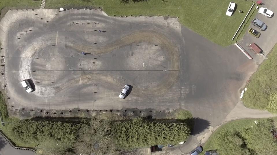 an aerial shot of two cars doing a figure-8 on a driving course