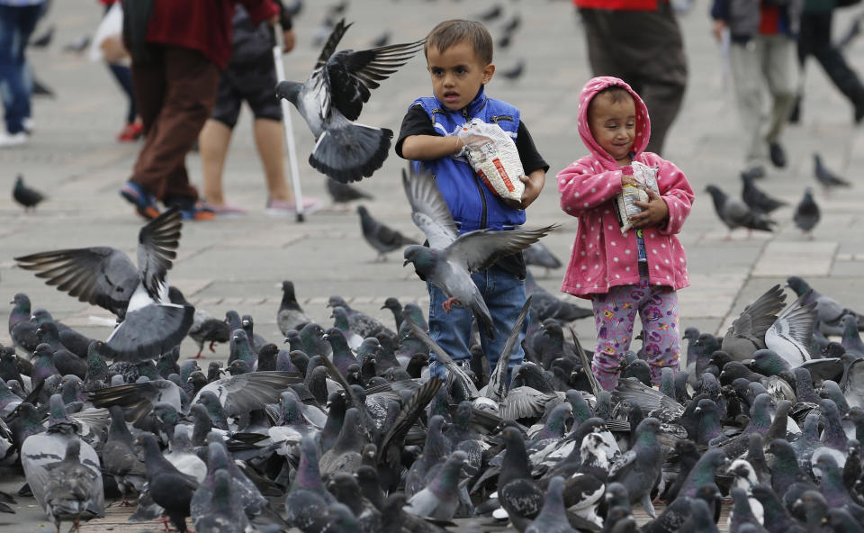 Children feed pigeons at Bolivar Square in Bogota, Colombia, Tuesday, Oct. 2, 2018. Officials believe that if people stop nourishing the birds, they will stop concentrating in public squares where their droppings sully historical buildings and put people's health at risk, but convincing people not to give the birds food has proven tricky. (AP Photo/Fernando Vergara)