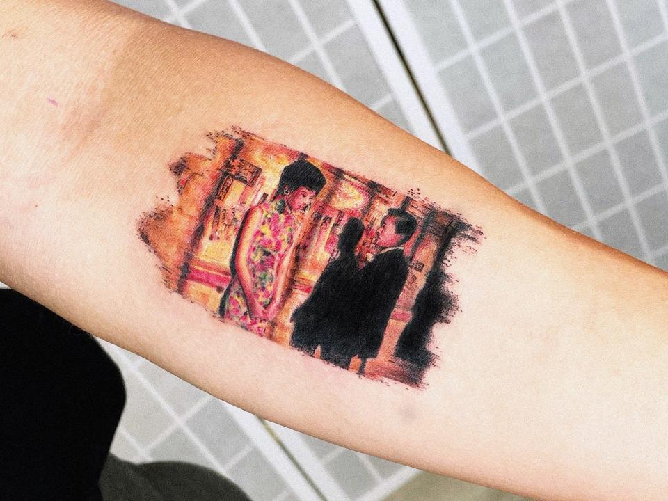 A colorful tattoo of two people on someone's forearm in front of a white screen