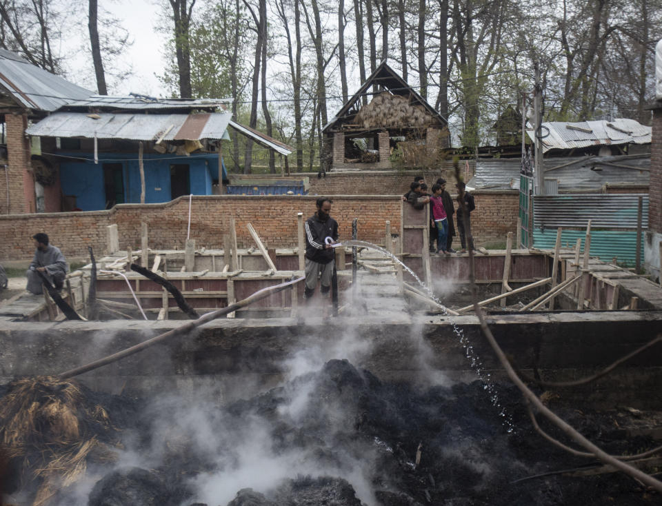 A Kashmiri man tries to douse the fire after fodder caught fire during a gun battle between government forces and suspected rebels in Bijbehara, some 28 miles (45 kilometers) south of Srinagar, Indian controlled Kashmir, Sunday, April 11, 2021. (AP Photo/Mukhtar Khan)