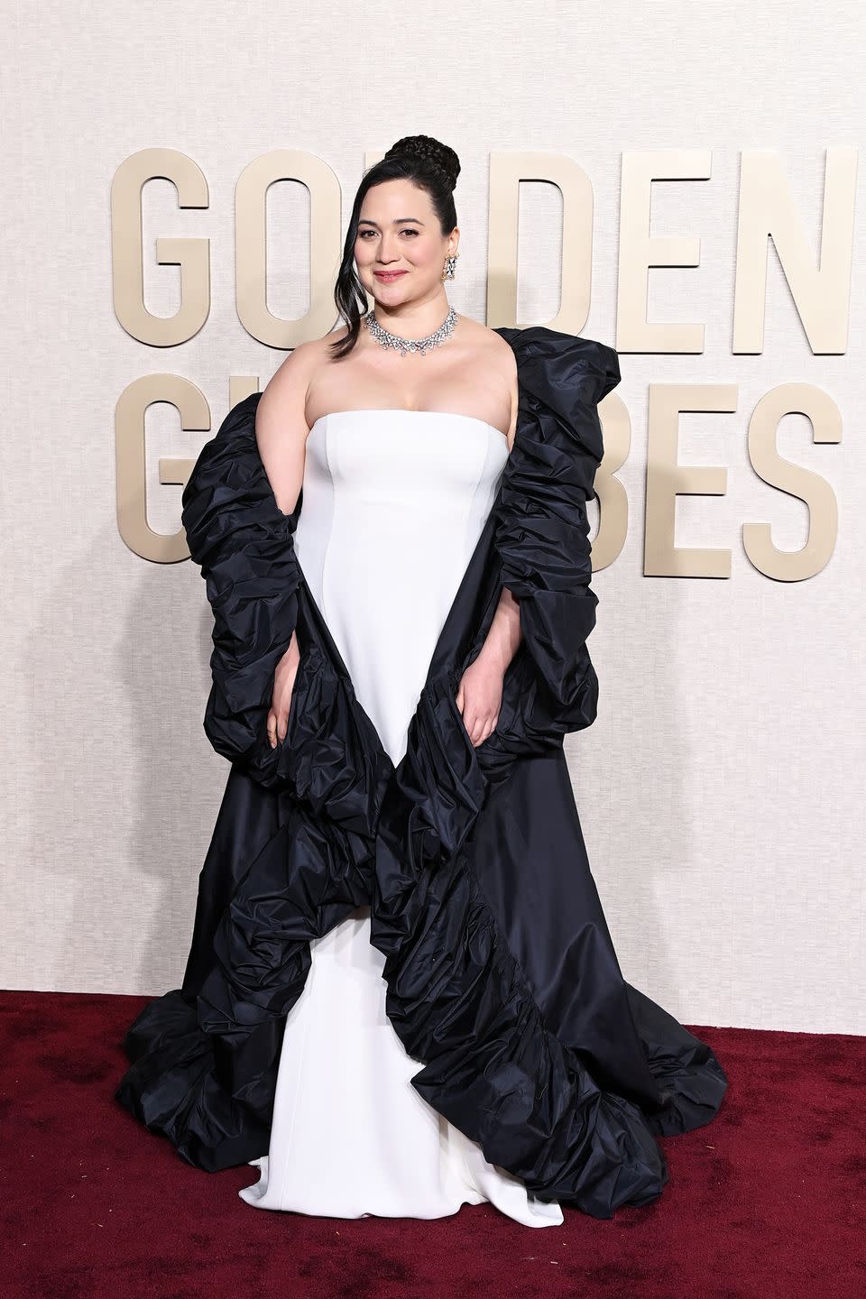 lily gladstone wearing a white dress and black coat at the golden globes