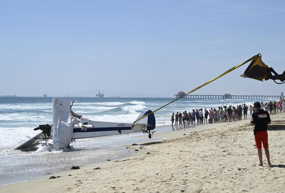 People look at a small plane that was pulled from the water after it crashed into the ocean in Huntington Beach, Calif., Friday, July 22, 2022. The plane towing a banner crashed in the ocean Friday during a lifeguard competition that turned into a real-life rescue along the popular beach. (Brittany Murray/The Orange County Register via AP)
