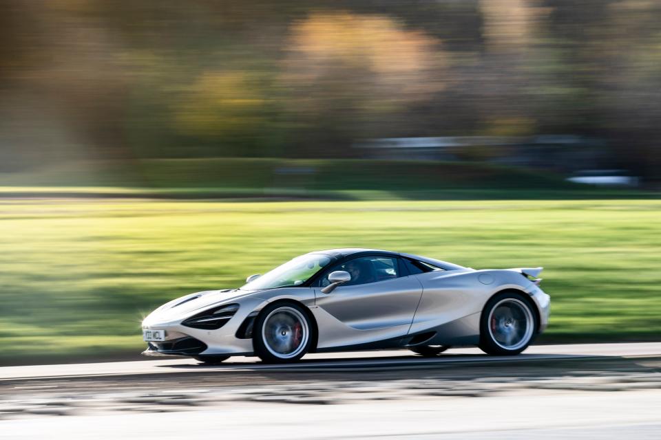 A silver McLaren 720S on a wooded road.