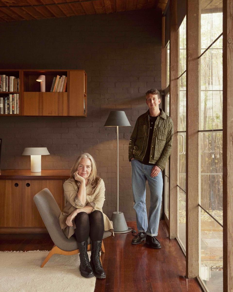 a man and woman standing in a room with a wood floor and a bookcase