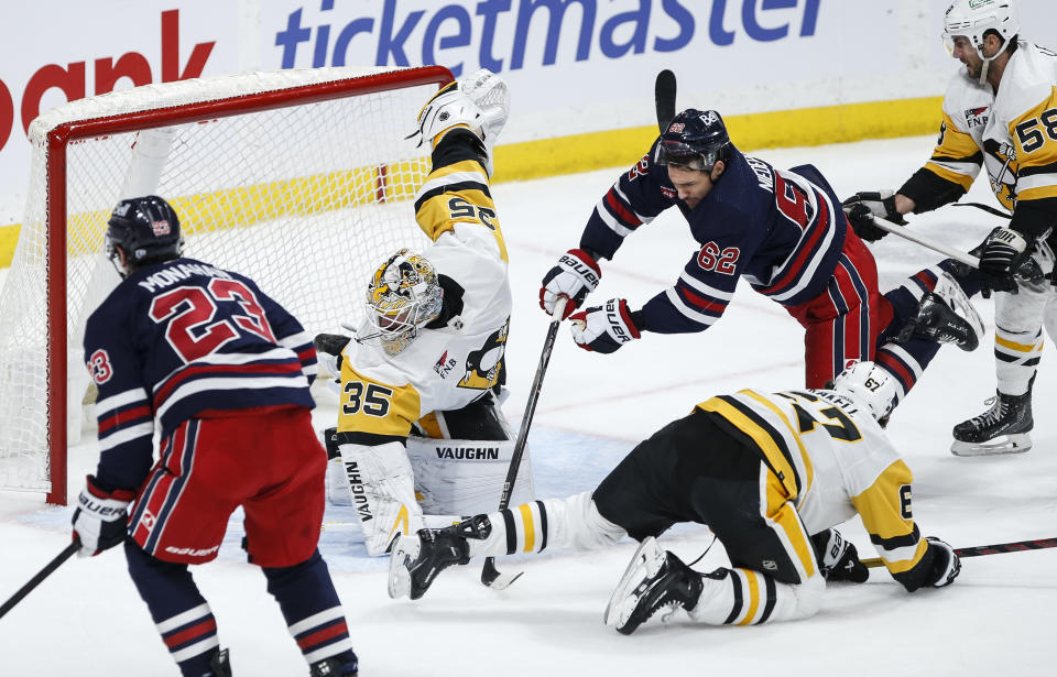 Pittsburgh Penguins goaltender Tristan Jarry (35) makes a save against Winnipeg Jets' Sean Monahan (23) as Penguins' Kris Letang (58) defends against Jets' Nino Niederreiter (62) during the third period of an NHL hockey game Saturday, Feb. 10, 2024, in Winnipeg, Manitoba. (John Woods/The Canadian Press via AP)