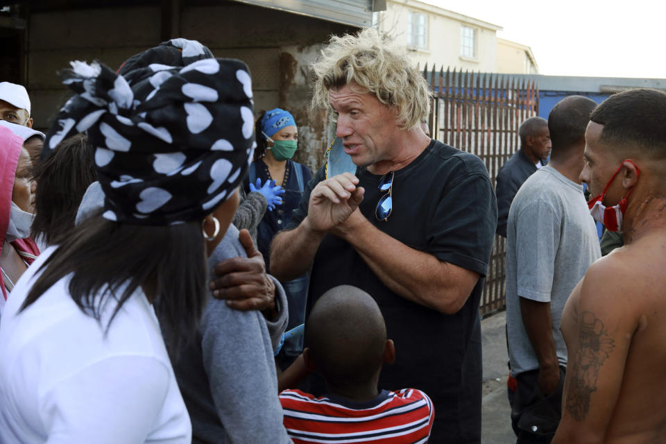 In this May 2, 2020, photo, preacher Andie Steele-Smith speaks to residents of the Manenberg neighborhood of Cape Town, South Africa. Steele-Smith recruited gang members to deliver food to homes and soup kitchens in the neighborhood during the coronavirus lockdown. (AP Photo/Nardus Engelbrecht)