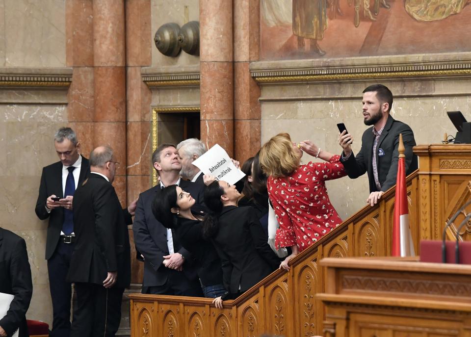 Deputy of the Hungarian Socialist Party (MSZP) Agnes Kunhalmi holds up a sheet that reads 'You succumbed to the multinational corporations' among other oppositional lawmakers as they block the steps leading to the rostrum at the start of the plenary session of the parliament in Budapest, Hungary, Wednesday, Dec. 12, 2018. (Lajos Soos/MTI via AP)