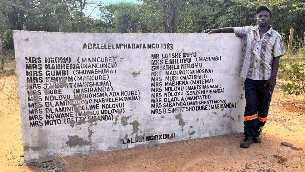Thabani Dhlamini by a memorial wall to those who were killed in his village of Salankomo by Zimbabwean soldiers in 1983