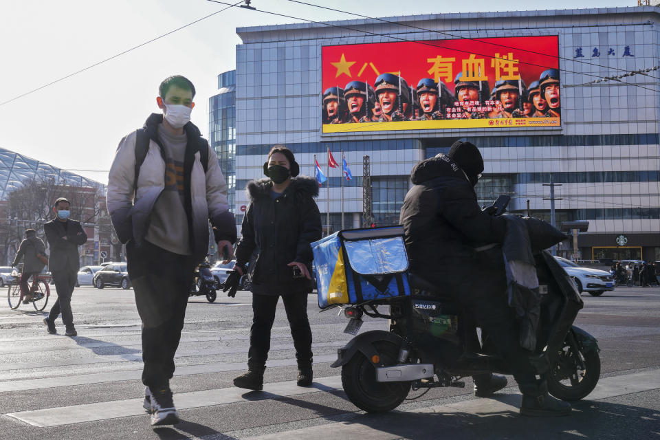 People walk across a street near a large screen promoting the Chinese People's Liberation Army carrying the words "Bloody" outside a mall in Beijing, Monday, Jan. 9, 2023. The Chinese military held large-scale joint combat strike drills starting Sunday, sending war planes and navy vessels toward Taiwan, both the Chinese and Taiwanese defense ministries said. (AP Photo/Andy Wong)