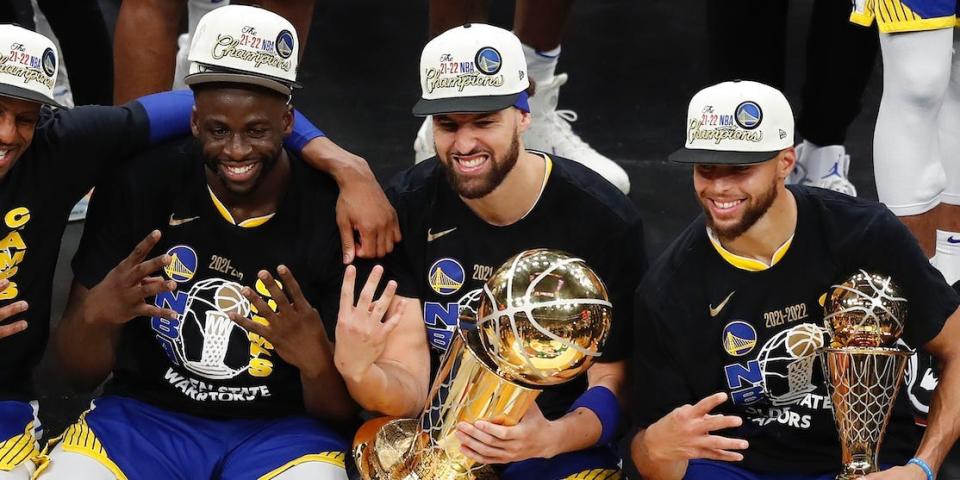 Andre Iguodala, Draymond Green, Stephen Curry, and Klay Thompson sit on a stage next to each other and hold up four fingers.