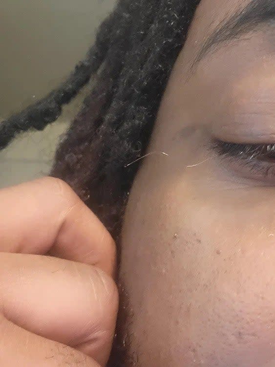 A person holding out a very long, curly, blonde eyelash from their eye