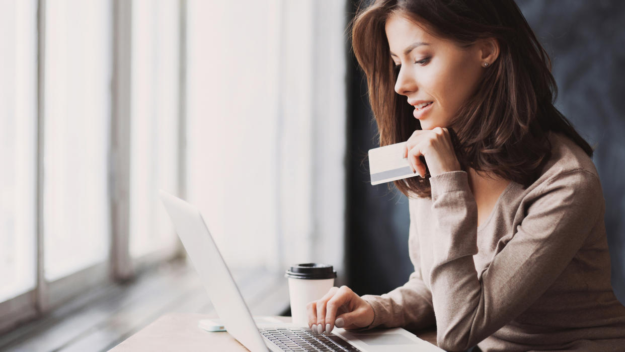 Young woman holding credit card and using laptop computer.