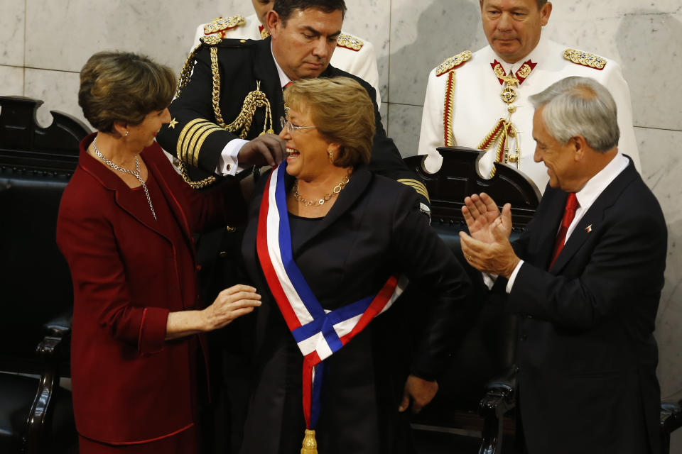 Chile's new President Michelle Bachelet, center, receives the presidential sash from Senate President Isabel Allende, left, after being sworn in during a ceremony before congress in Valparaiso, Chile, Tuesday, March 11, 2014. Standing next to Bachelet applauding is outgoing President Sebastian Pinera. (AP Photo/Victor R. Caivano)