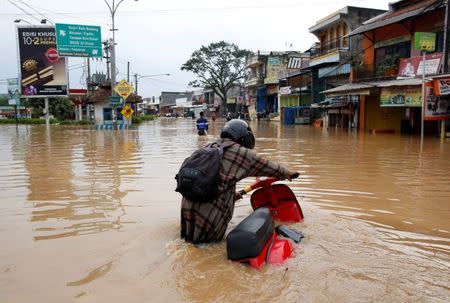 A woman pushes her scooter down a flooded street after heavy seasonal rains caused the Citarum river to flood in Dayeuhkolot, south of Bandung, West Java province, Indonesia, February 23, 2018. REUTERS/Darren Whiteside