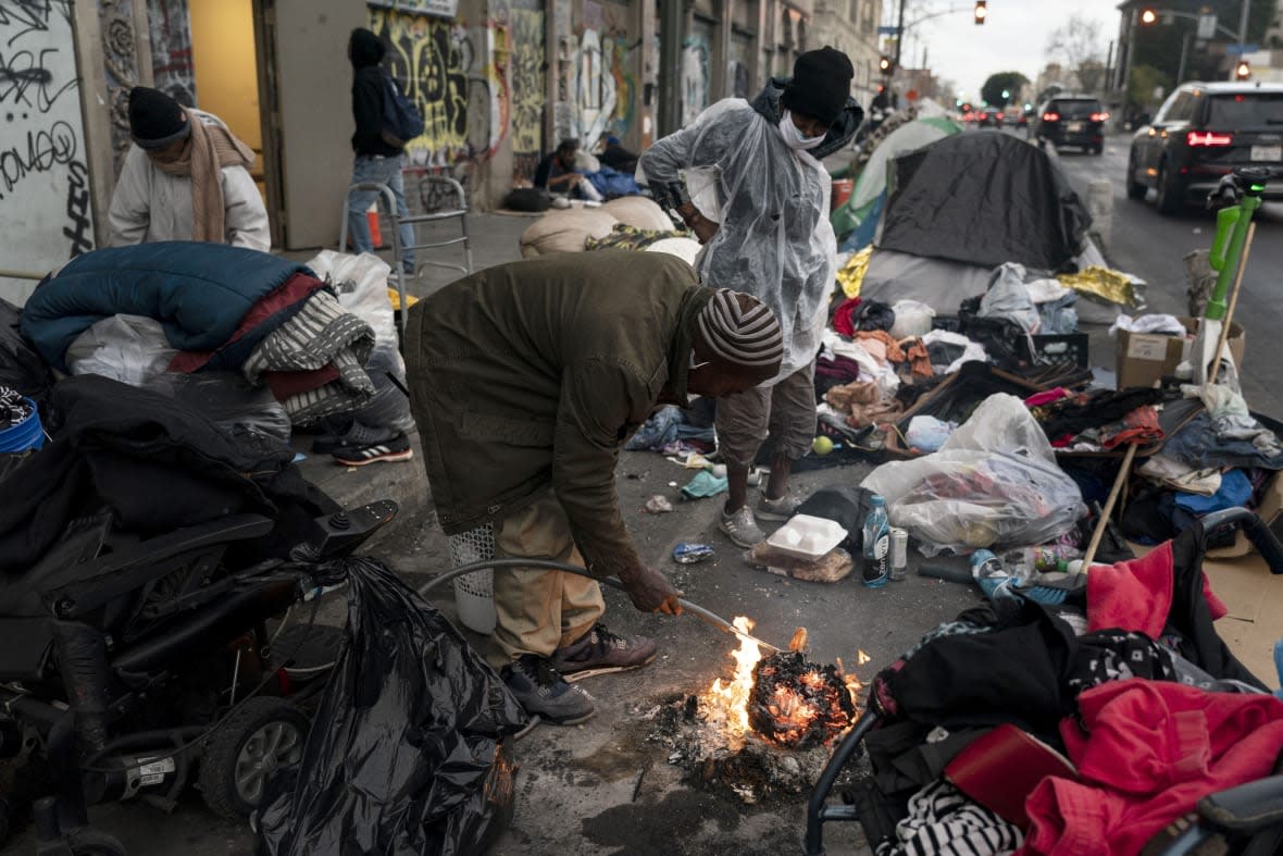 Robert Mason, a 56-year-old homeless man, warms up a piece of doughnut over a bonfire he set to keep himself warm on Skid Row in Los Angeles, on Feb. 14, 2023. (AP Photo/Jae C. Hong, File)