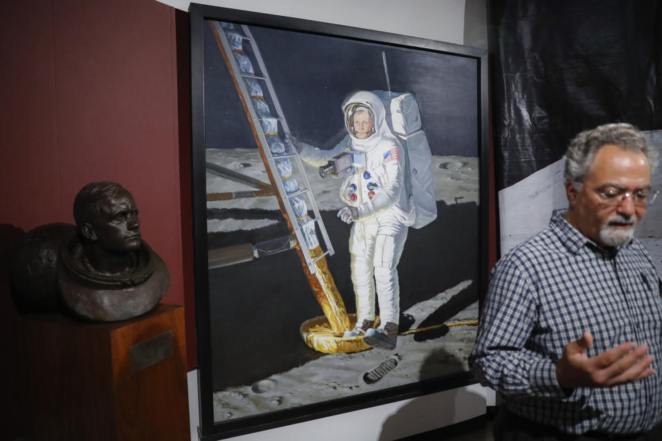 A portrait of astronaut Neil Armstrong stepping onto the surface of the moon is displayed behind museum director Dante Centuori, right, at the Armstrong Air & Space Museum, Wednesday, June 26, 2019, in Wapakoneta, Ohio. Neil Armstrong helped put Wapakoneta on the map July 20, 1969, when he became the first human to walk on the moon. The late astronaut remains larger than life in the city 60 miles (96.56 kilometers) north of Dayton, where visitors are greeted by the space base-shaped top of the space museum named for him as they exit Interstate 75. (AP Photo/John Minchillo)