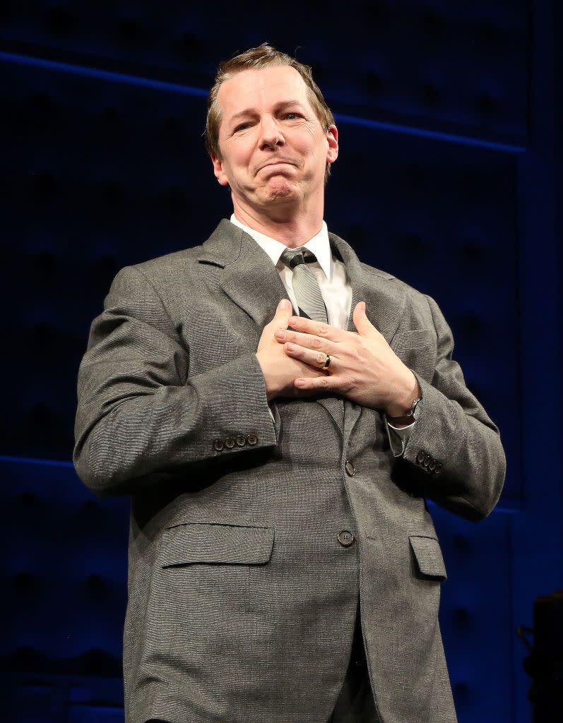 sean hayes wearing a gray suit, holding his hands against his chest and smiling, looking off camera