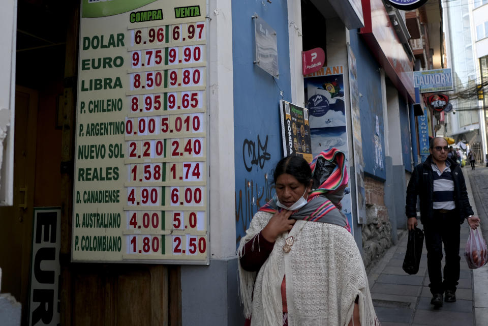 A woman walks by a sign showing the currency exchange rate in La Paz, Bolivia, Friday, June 28, 2024, two days after Army troops stormed the government palace in what President Luis Arce called a coup attempt. (AP Photo/Carlos Sanchez)