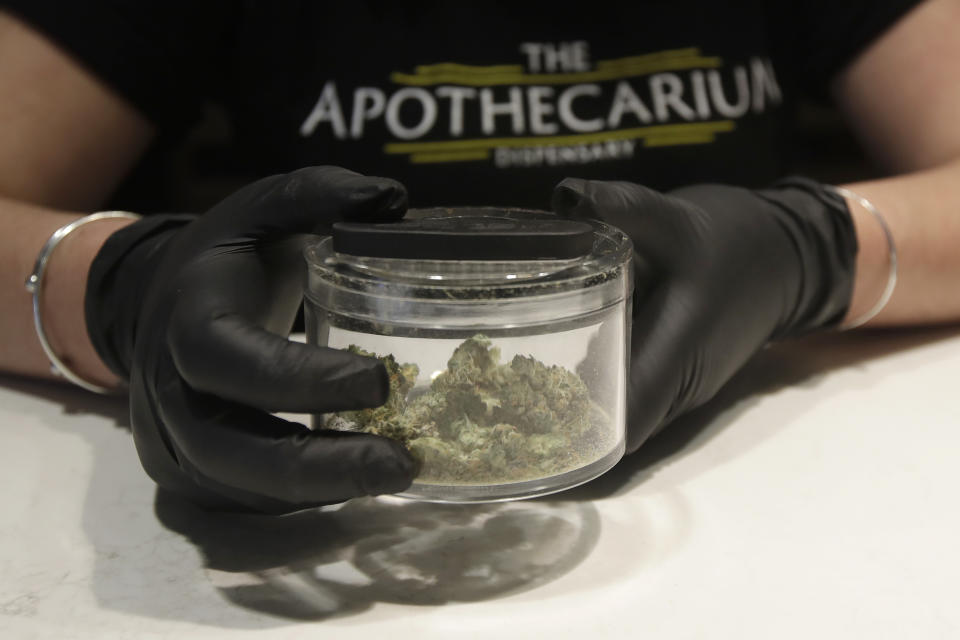 Cali Manzello, general manager at The Apothecarium cannabis dispensary, wears gloves when holding a marijuana sample for smelling while posing for photos at the store in San Francisco, Wednesday, March 18, 2020. As about 7 million people in the San Francisco Bay Area are under shelter-in-place orders, only allowed to leave their homes for crucial needs in an attempt to slow virus spread, marijuana stores remain open and are being considered "essential services." (AP Photo/Jeff Chiu)