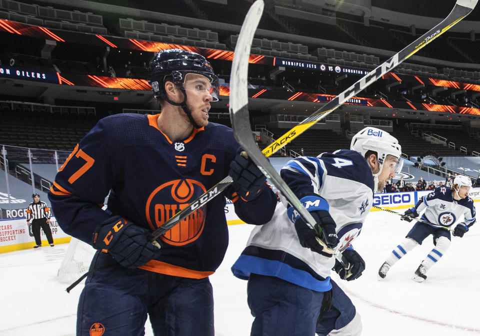 Edmonton Oilers' Connor McDavid (97) and Winnipeg Jets' Neal Pionk (4) work in the corner during the second period of an NHL hockey game Wednesday, Feb. 17, 2021, in Edmonton, Alberta. (Jason Franson/The Canadian Press via AP)