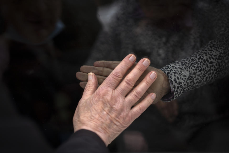 Javier Anto, 90, and his wife Carmen Panzano, 92, touch hands through the window separating the nursing home from the street in Barcelona, Spain, Wednesday, April 21, 2021. Since the pandemic struck, a glass pane has separated _ and united _ Javier and Carmen for the first prolonged period of their six-decade marriage. Anto has made coming to the street-level window that looks into the nursing home where his wife, since it was closed to visits when COVID-19 struck Spain last spring. (AP Photo/Emilio Morenatti)