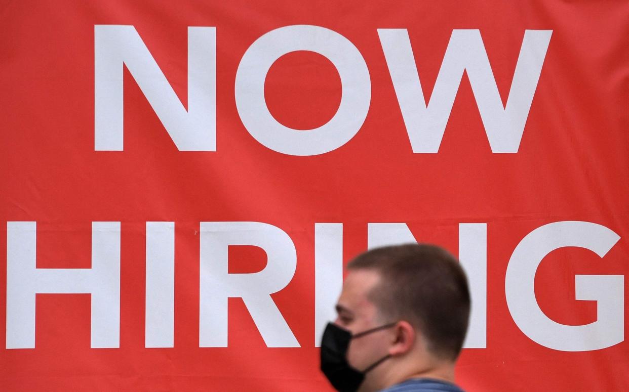 A man walks by a ‘Now Hiring’ sign