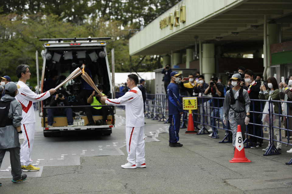 An Olympic torch relay runner, center, hands over the flame of the torch to the next runner during the first day of the Osaka round at a former Expo site in Suita, north of Osaka, western Japan, Tuesday, April 13, 2021. The Tokyo 2020 Olympic kick-off event which was rescheduled due to the coronavirus outbreak was yet rearranged to hold at the former Expo park, instead of public streets, to close off the audience from the even, following the mayor's decision as Osaka has had sharp increases in daily cases since early March. (AP Photo/Hiro Komae)