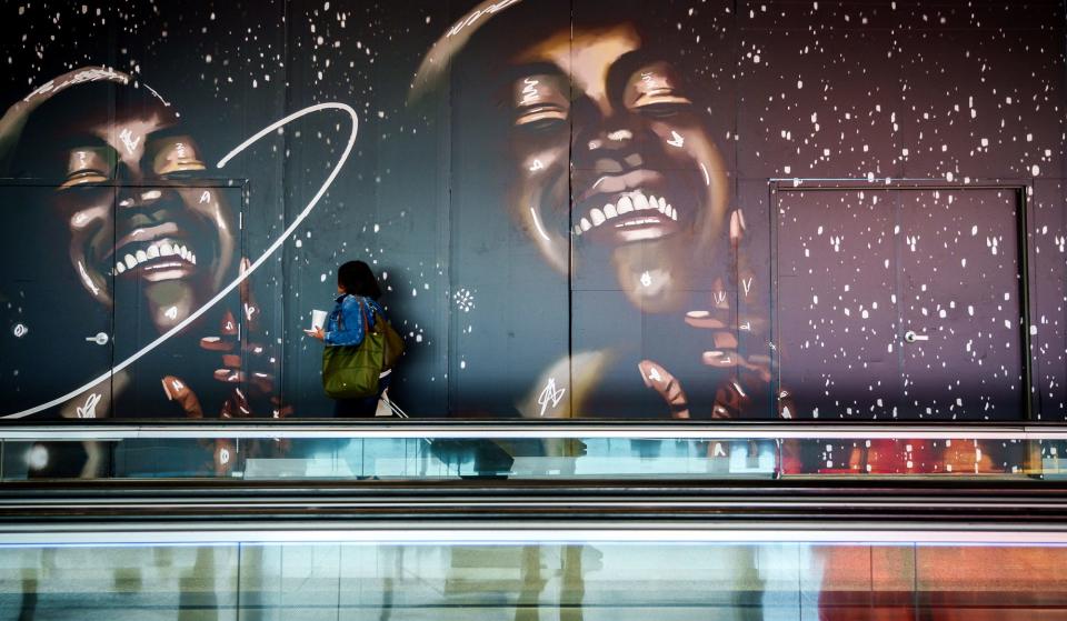 An air traveler carrying food and drink passes by a temporary wall, with accompanying local artwork by Boxx the Artist, that separates patrons Wednesday, Nov. 9, 2022, from the construction of a new Ben's Soft Pretzels location inside Indianapolis International Airport. The Goshen-based business serves handcrafted, fresh Amish-inspired jumbo soft pretzels.