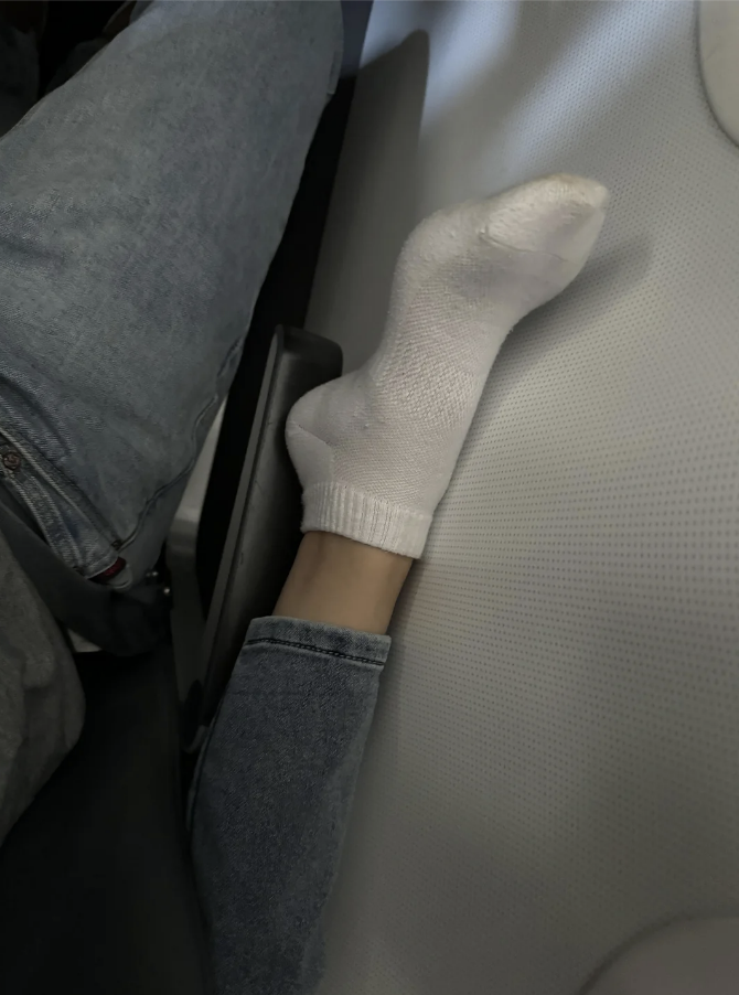 Person's foot in a white sock resting on an airplane seat divider