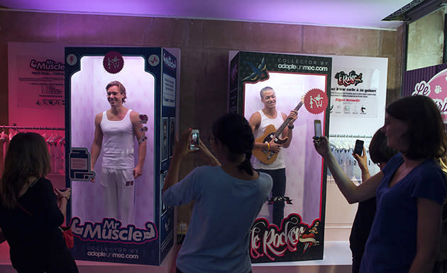 Women gather and take pictures in front of boxes where men stand like toys, on September 11, 2012 in Paris, on the opening day of a store of the online dating site 