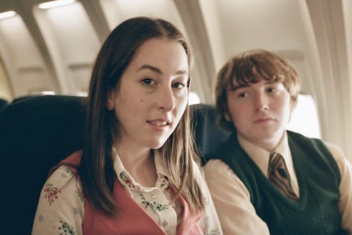A girl and boy sit next to each other on a plane.