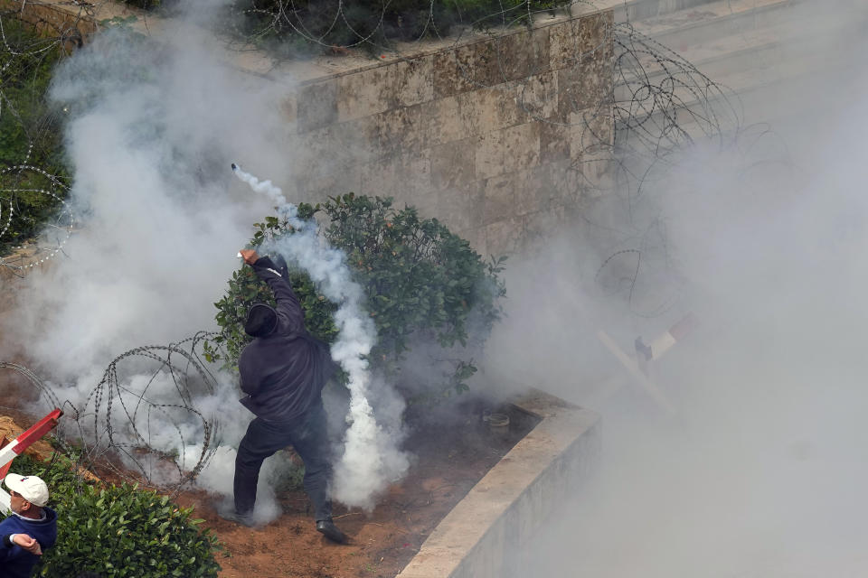 A retired army soldier throws back a tear gas canister towards riot policemen during a protest demanding better pay, in Beirut, Lebanon, Wednesday, March 22, 2023. Lebanese security forces fired tear gas to disperse hundreds of protesters who tried to break through the fence leading to the government headquarters in downtown Beirut Wednesday amid widespread anger over the harsh economic conditions in the country. (AP Photo/Bilal Hussein)