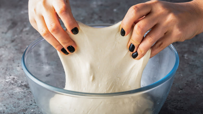 Someone stretching dough in bowl