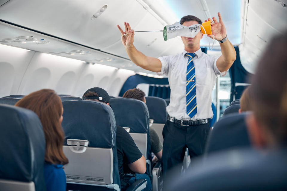 Waist up portrait of steward showing the safety rules and instructions for using oxygen masks in the commercial airplane