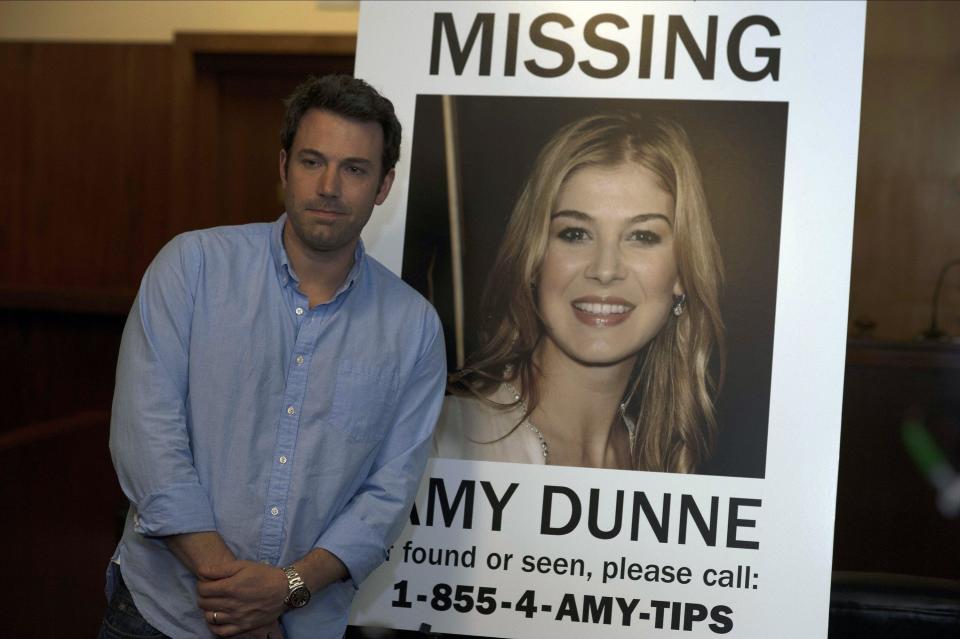 A man smiles next to a missing woman poster