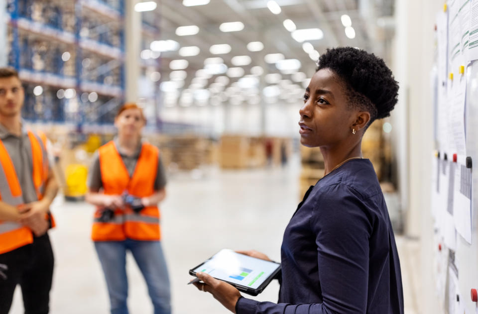 employees  Supervisor standing by a whiteboard with a digital tablet discussing dispatch plan with workers.  Team of workers having meeting in a distribution warehouse.