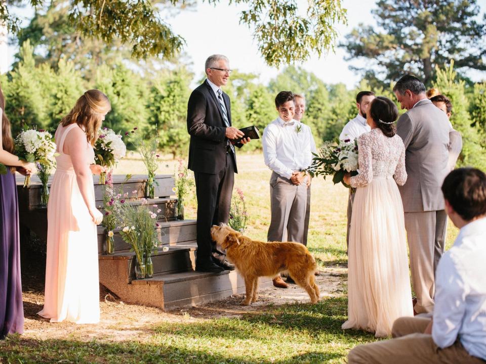 A bride and groom stand in front of their wedding altar with their dog ahead of them.