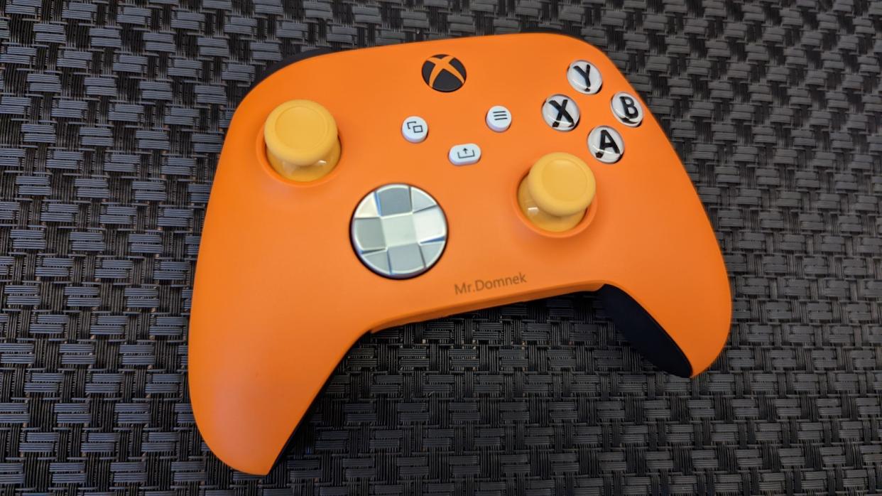 An orange coloured Xbox controller with custom orange thumbsticks and white buttons on a black patterned surface from the Xbox Design Lab. (Photo: Yahoo Gaming SEA)