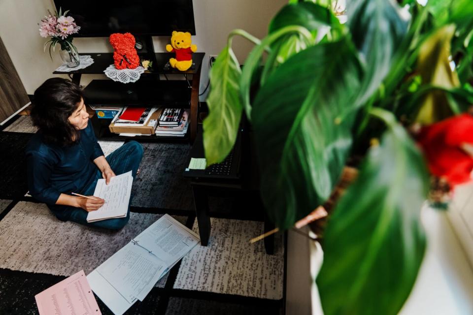 A woman seated on the floor holds papers and a pencil