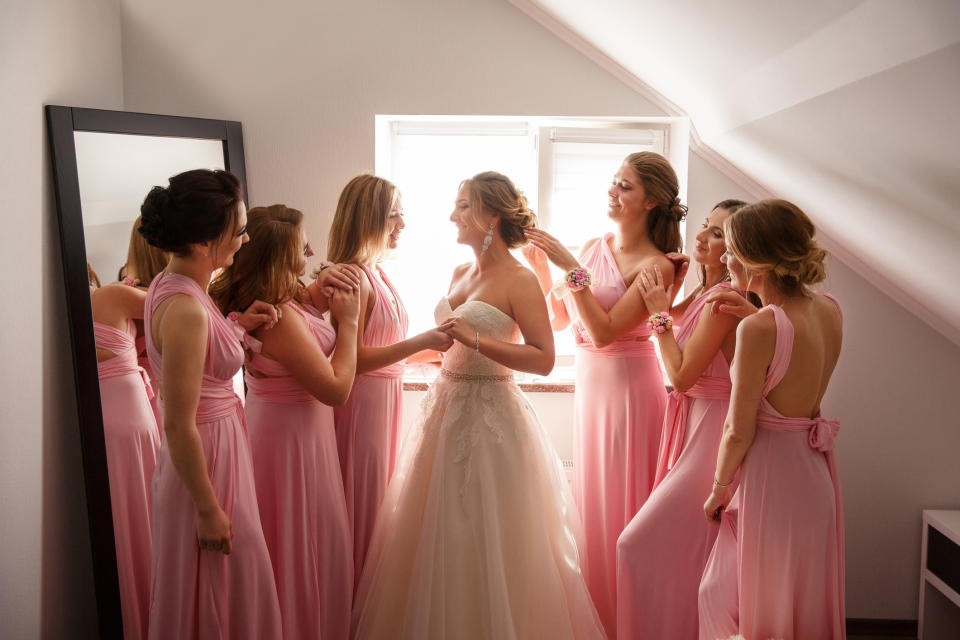 A bride smiles in her dress as she is surrounded by bridesmaids