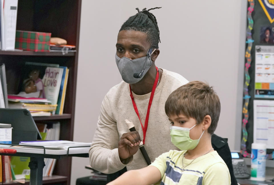 Elementary school music teacher Jami Brown, left, uses a mic to work with his class including third grader Walker Moore at Tibbals Elementary School in Murphy, Texas, Thursday, Dec. 3, 2020. Texas Gov. Greg Abbot's statewide mask order does not mandate face covering for children under the age of 10, allowing some school districts to not require masks for children leaving the choice of mask use up to the parents. (AP Photo/LM Otero)