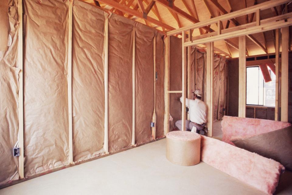 Person installing fiberglass insulation on the walls of an unfinished room, with construction materials around