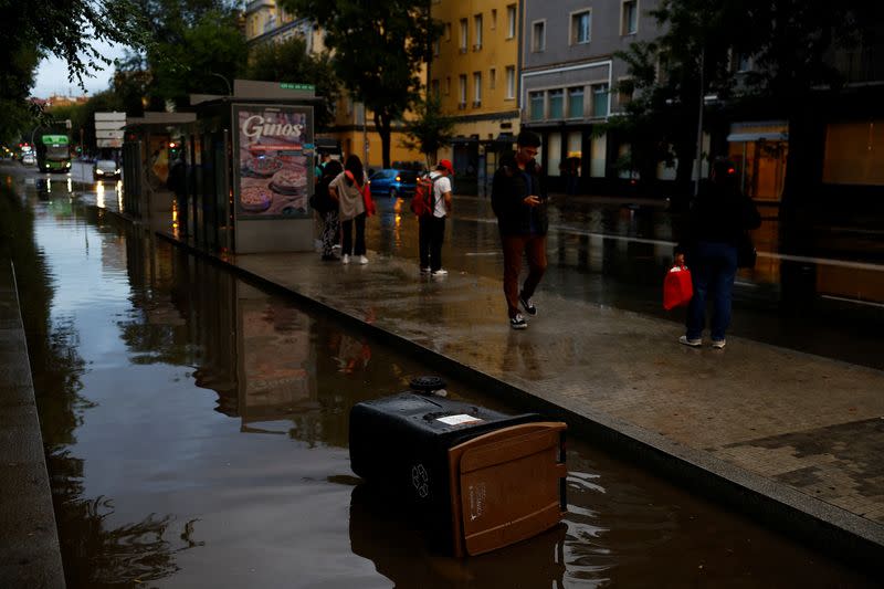 Personas esperan el autobús junto a una carretera inundada por las fuertes lluvias en Madrid