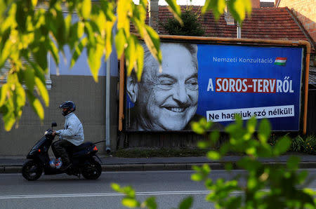 FILE PHOTO: A man rides his moped past a government billboard displaying George Soros in monochrome next to a message urging Hungarians to take part in a national consultation about what it calls a plan by the Hungarian-born financier to settle a million migrants in Europe per year, in Szolnok, Hungary, October 2, 2017. REUTERS/Bernadett Szabo/File Photo