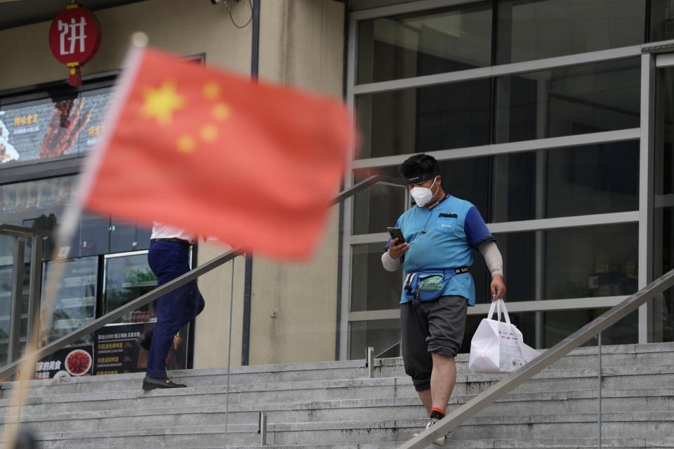 A delivery man walks near a Chinese flag after picking up an order at a mall in Beijing, Monday, Aug. 15, 2022. China’s central bank trimmed a key interest rate Monday to shore up sagging economic growth at a politically sensitive time when President Xi Jinping is believed to be trying to extend his hold on power. (AP Photo/Ng Han Guan)